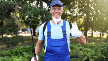 Worker with insecticide sprayer near green bush outdoors. Pest control